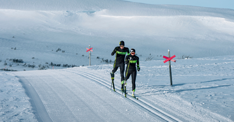 Dva lidé na běžkách jedou po zasněžené trase