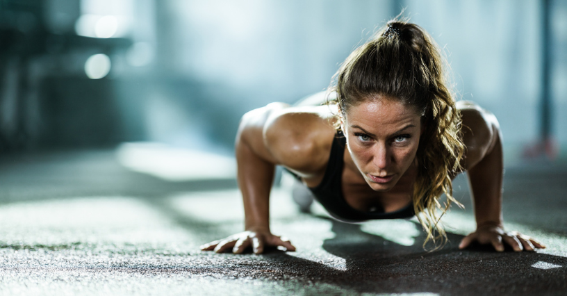 Žena trénuje kliky na podlaze v posilovně