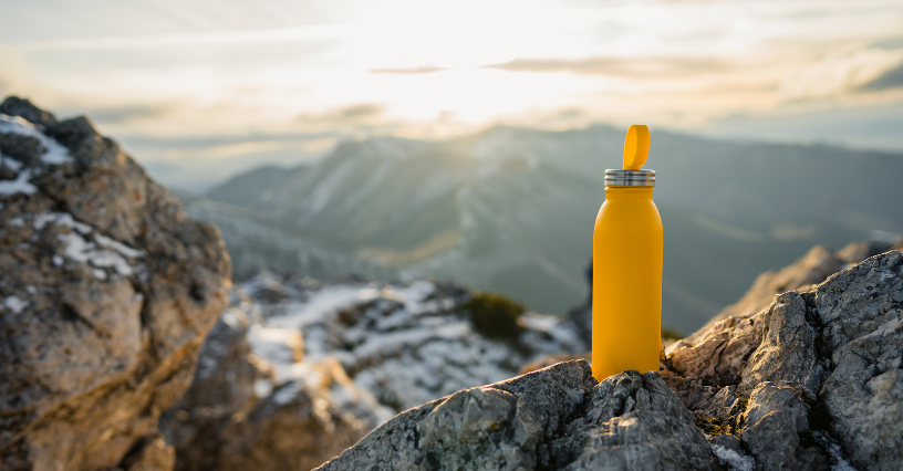 Žlutá láhev je umístěna na skalách s horským pozadím při západu slunce