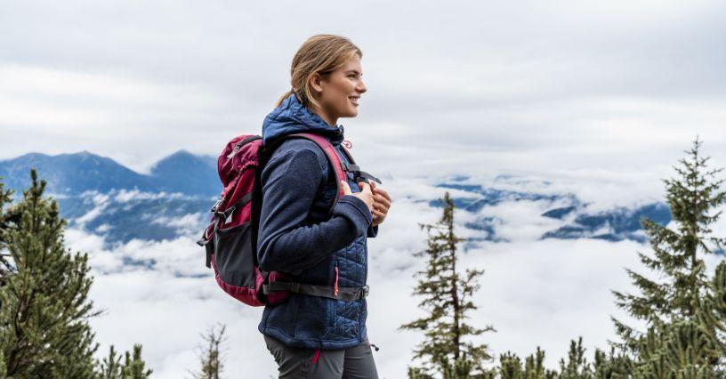 Žena s batohem stojí na horské stezce