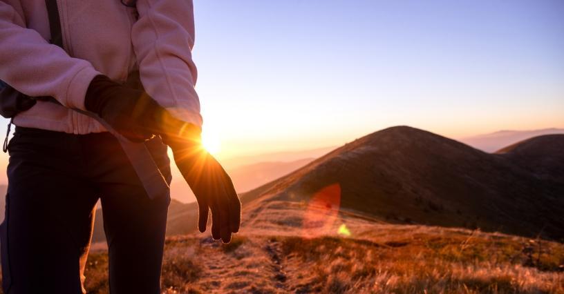 Osoba si natahuje rukavice při východu slunce na horách