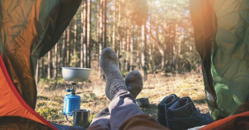 Pohled ze stanu na nohy v ponožkách, vařič a boty v lese