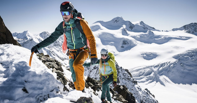 Dva horolezci stoupají po zasněženém svahu s vybavením na zádech